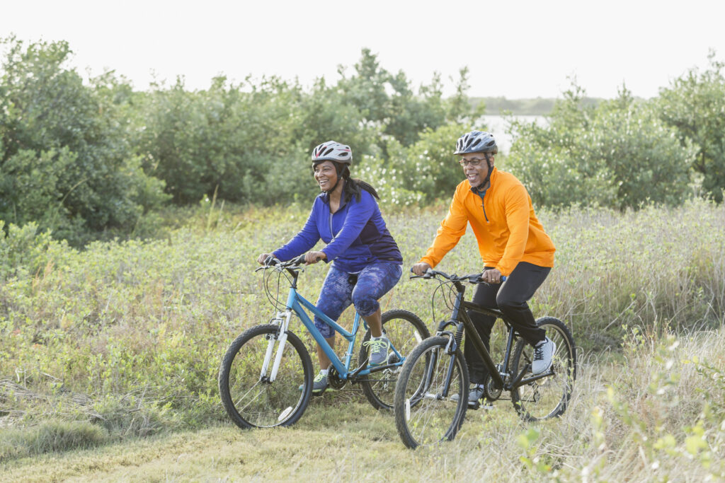 A couple riding mountain bikes in a state park. They are wearing helmets, cycling along a rural trail side by side.