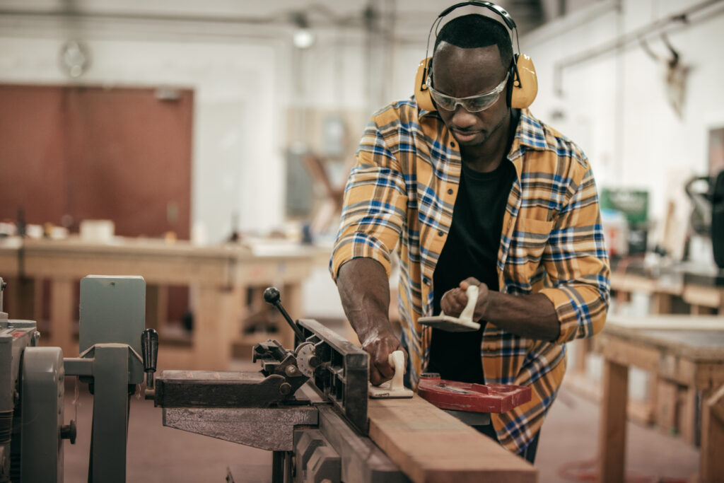 Male carpenter working with power tools in his wood shop. The man is wearing safety glasses and headphones.