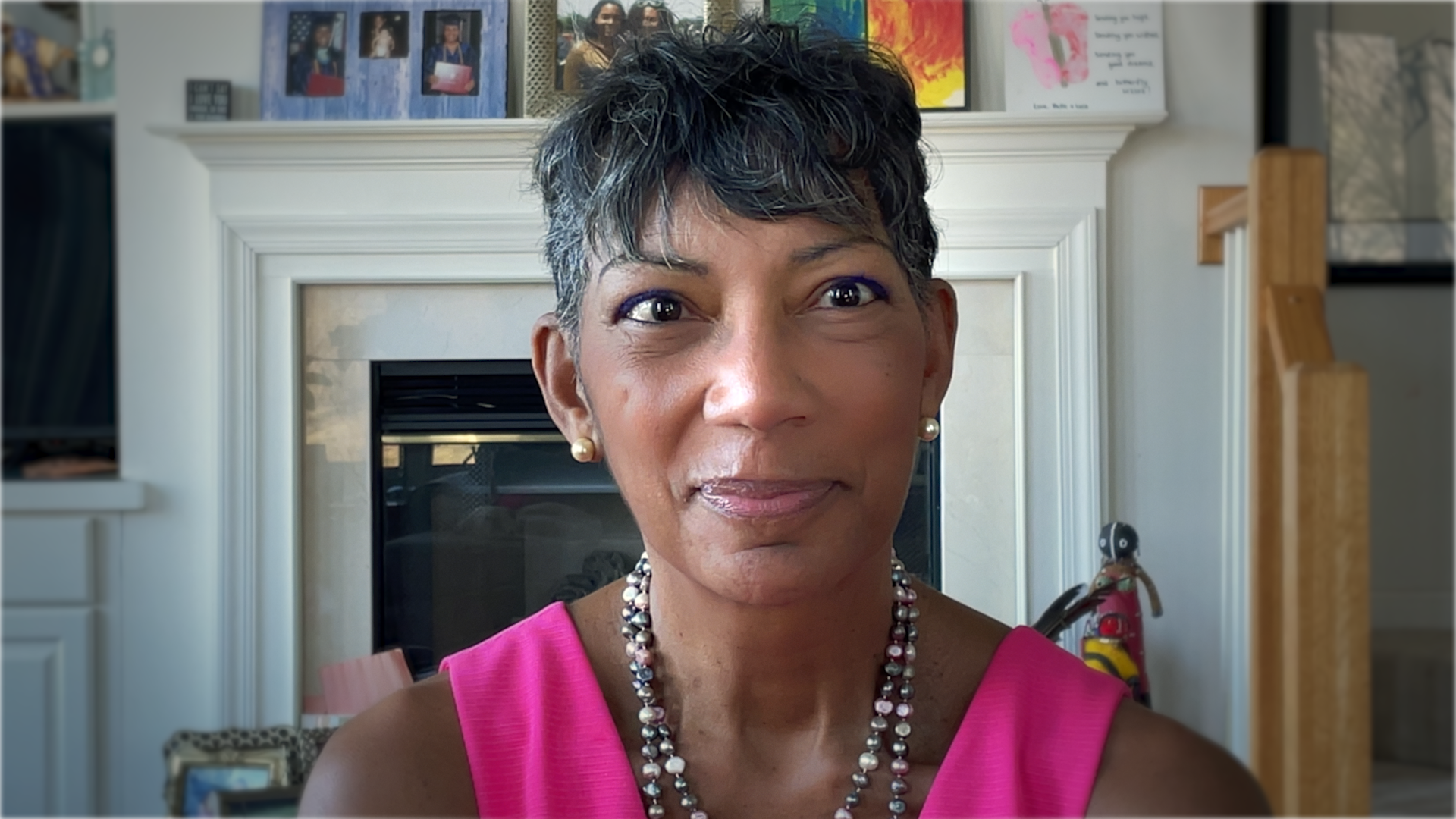 Ricki is an older Black woman with short hair, wearing earrings and a beaded necklace and pink shirt.
