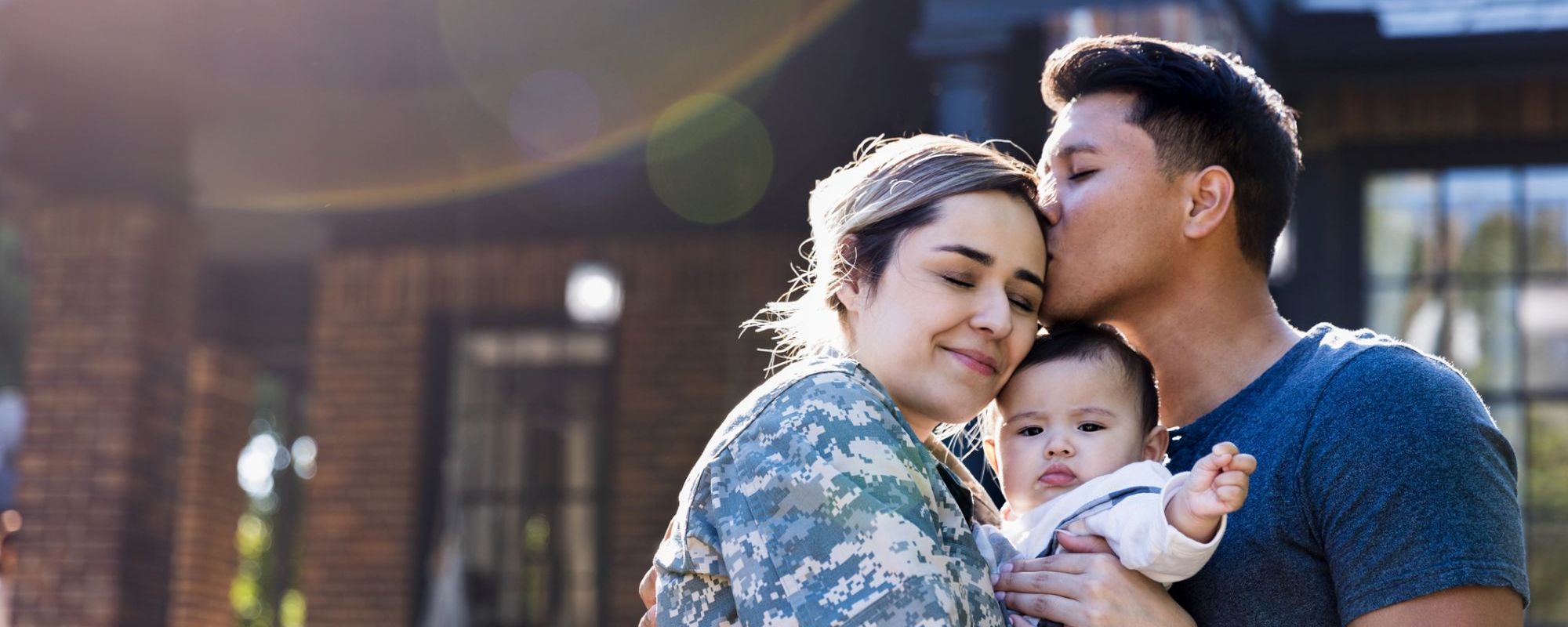 Woman in military uniform and father hugging baby.