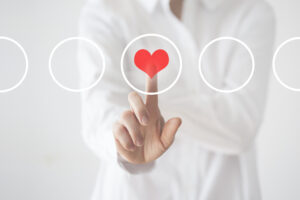 A person in a white coat touches a red heart in a circle as if on a screen.