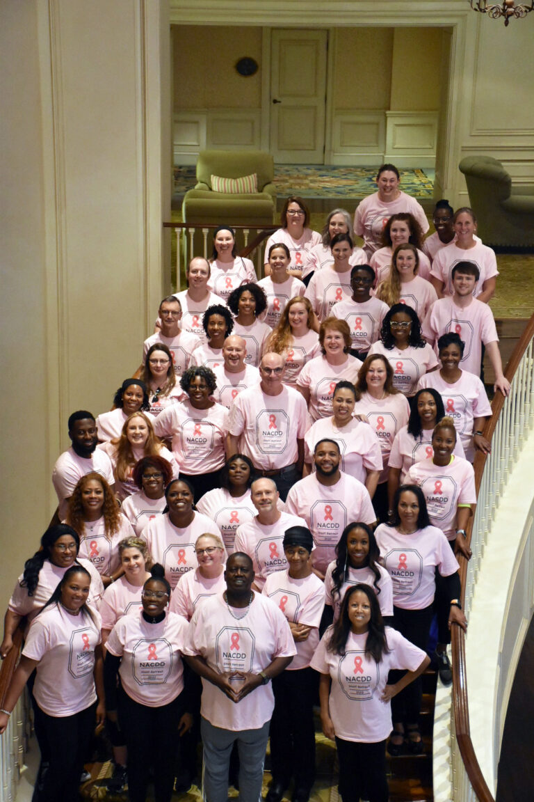 NACDD Staff Members are on a staircase wearing pink breast cancer awareness t-shirts.