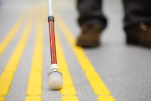 A white cane leads a person long a street with multiple yellow lines.