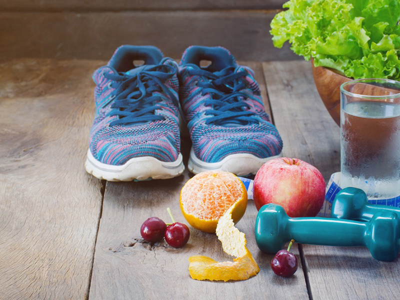 Shoes, various fruits, a glass of water, and weights, on a rustic wood floor.