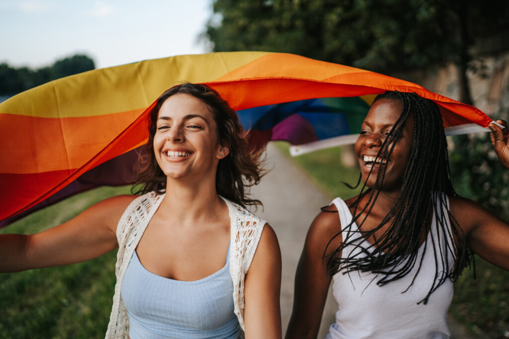 Young multi ethnic couple with rainbow flag walking in a city park