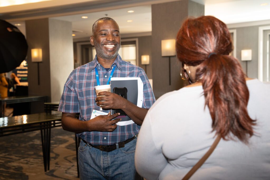 Man holding conference materials and coffee, smiling at a woman.