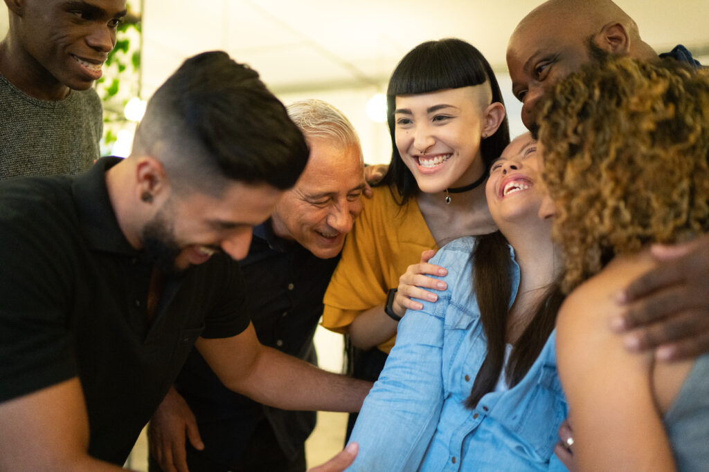 A group of people of different ages, sexes, and ethnicities with and without disabilities embracing.
