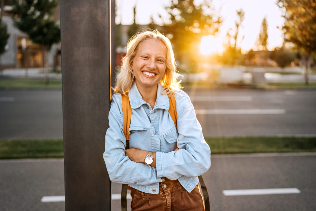 Young business woman stands against a telephone pole at sunset.