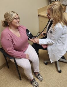 Patient in pink shirt sitting in chair with feet flat on the ground while doctor takes blood pressure reading in a clinical office 