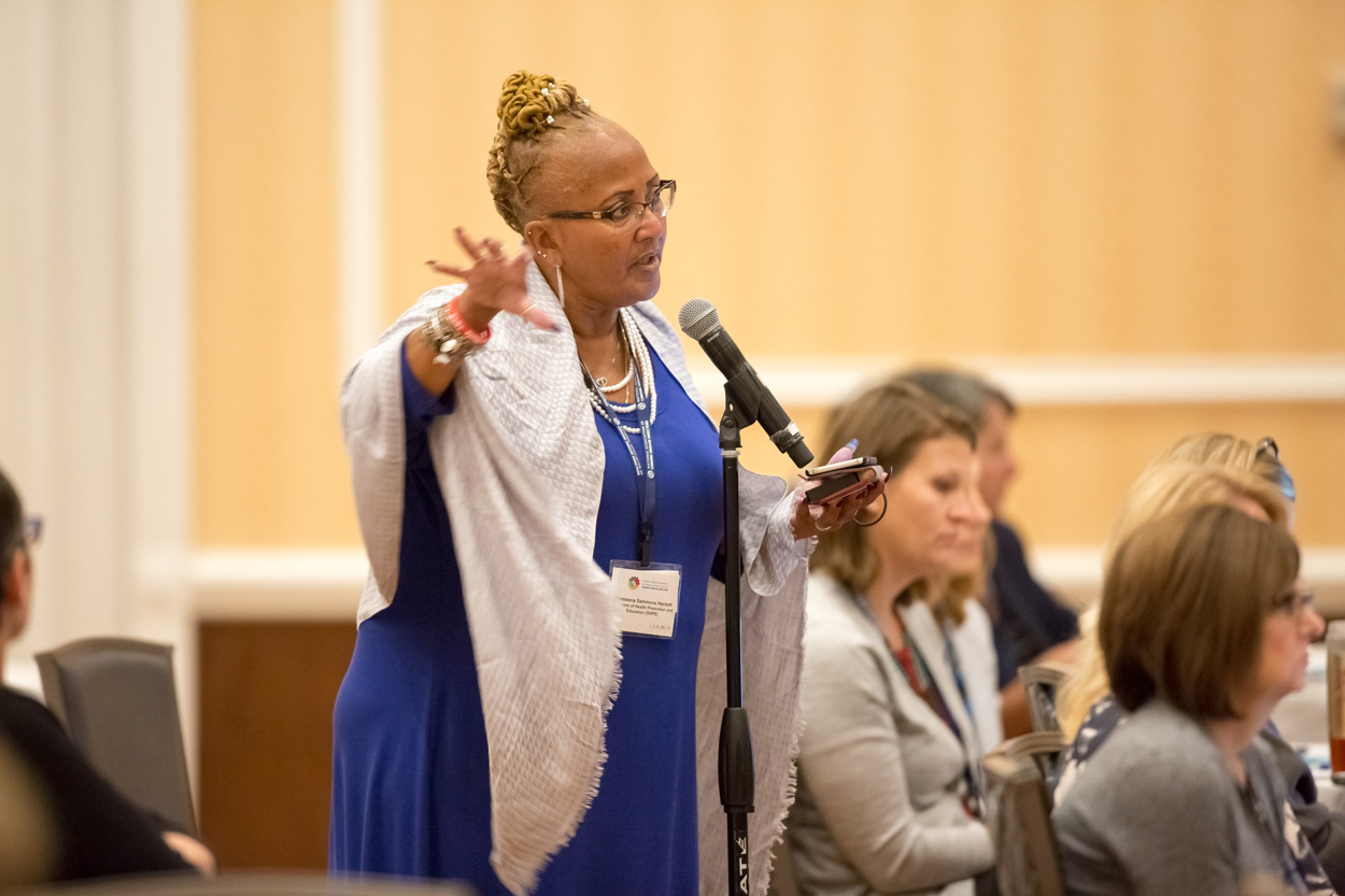 A woman stands at a microphone to ask a question during a conference presentation.