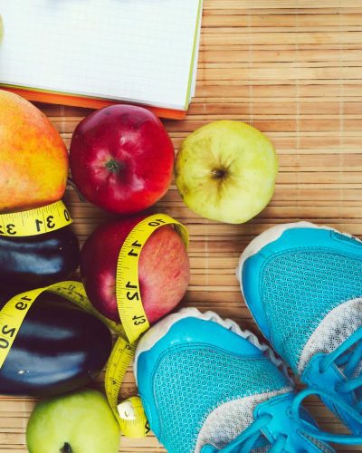 Various fruit, a tape measure, and shoes on a wood table.
