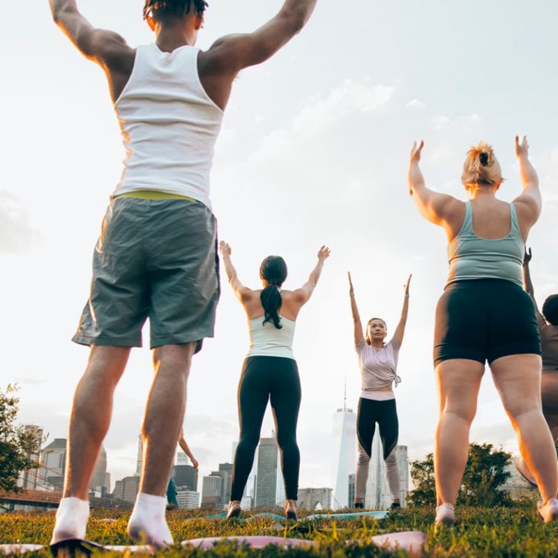 Instructor leads outdoor yoga at a park with city background at dawn