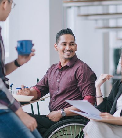 A man in a wheelchair smiles in conversation with coworkers.