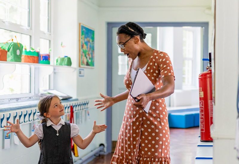 A teacher smiling at a child with joy at school.